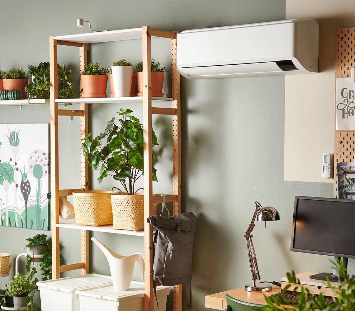 A living room with wooden book shelves, a desk and an air heat pump mounted on the wall.