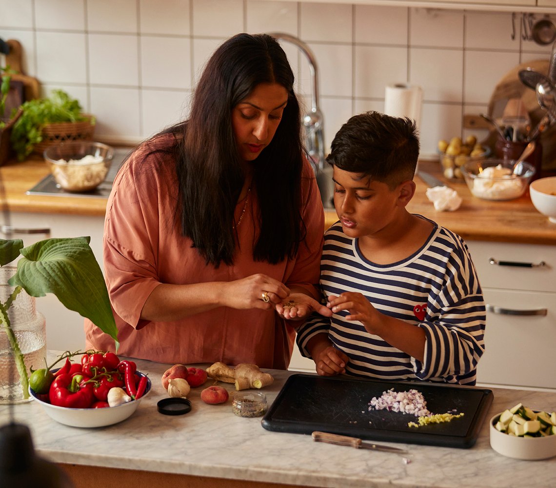 A woman and a boy preparing vegetables for a meal by a kitchen counter.
