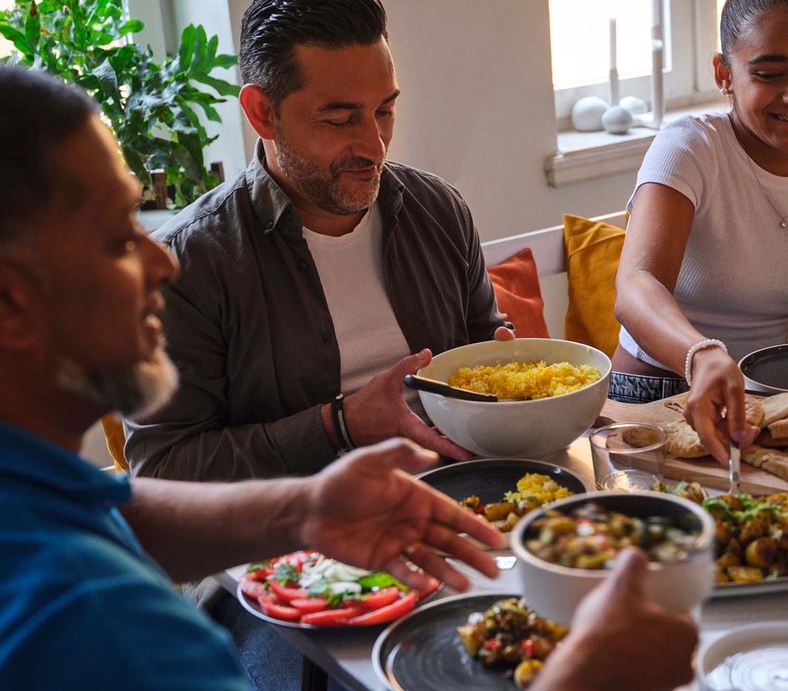 Three family members sitting by a dinner table passing bowl of food around.