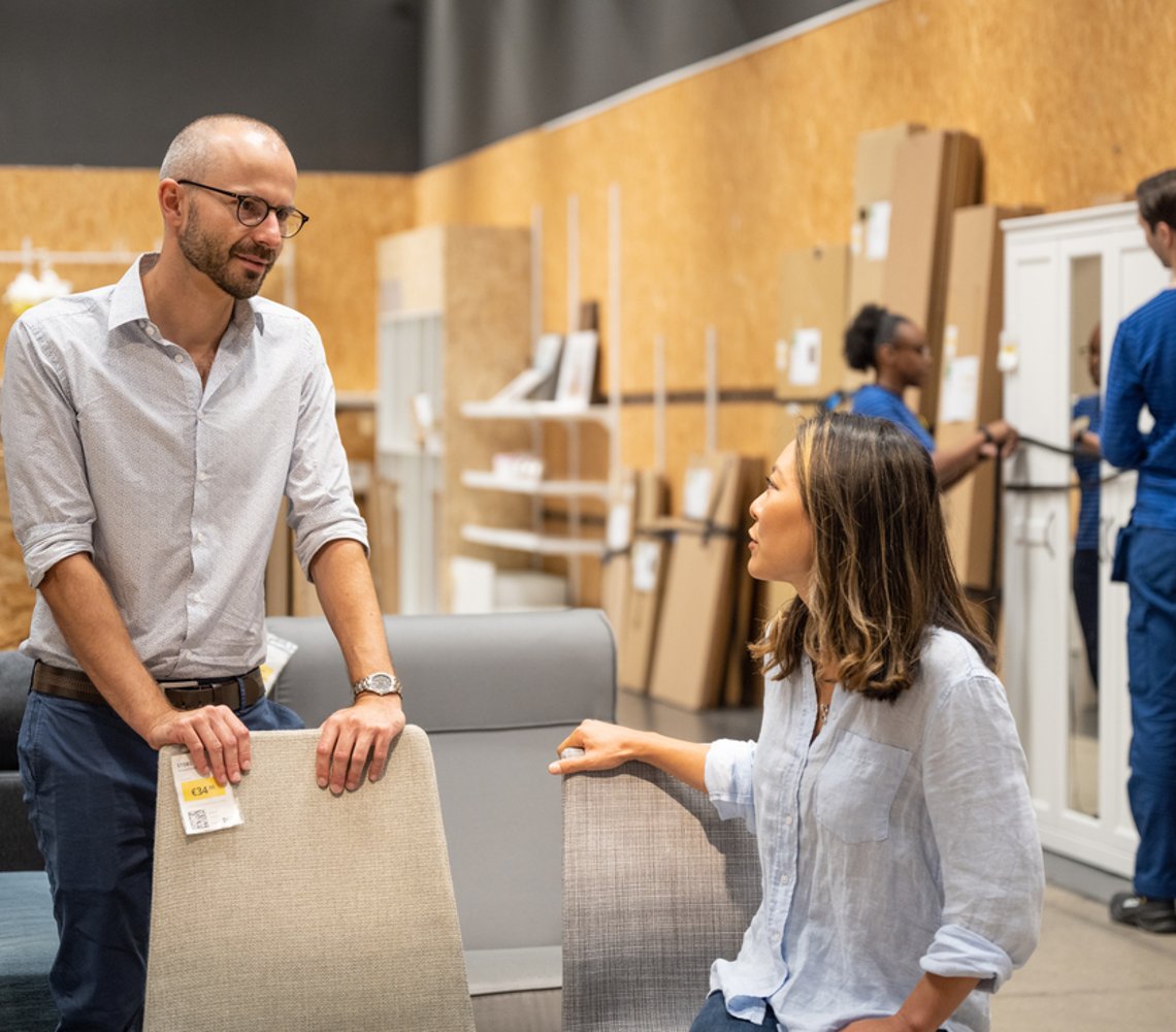 A man and a woman trying out chairs in the IKEA circular shop.