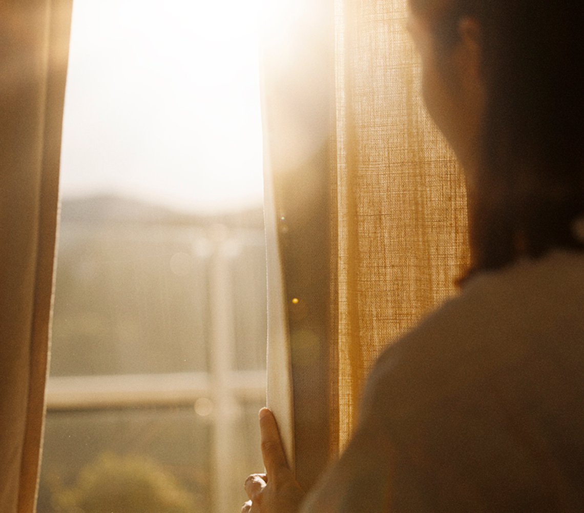 Woman pulling a curtain aside, while the sun is shining.