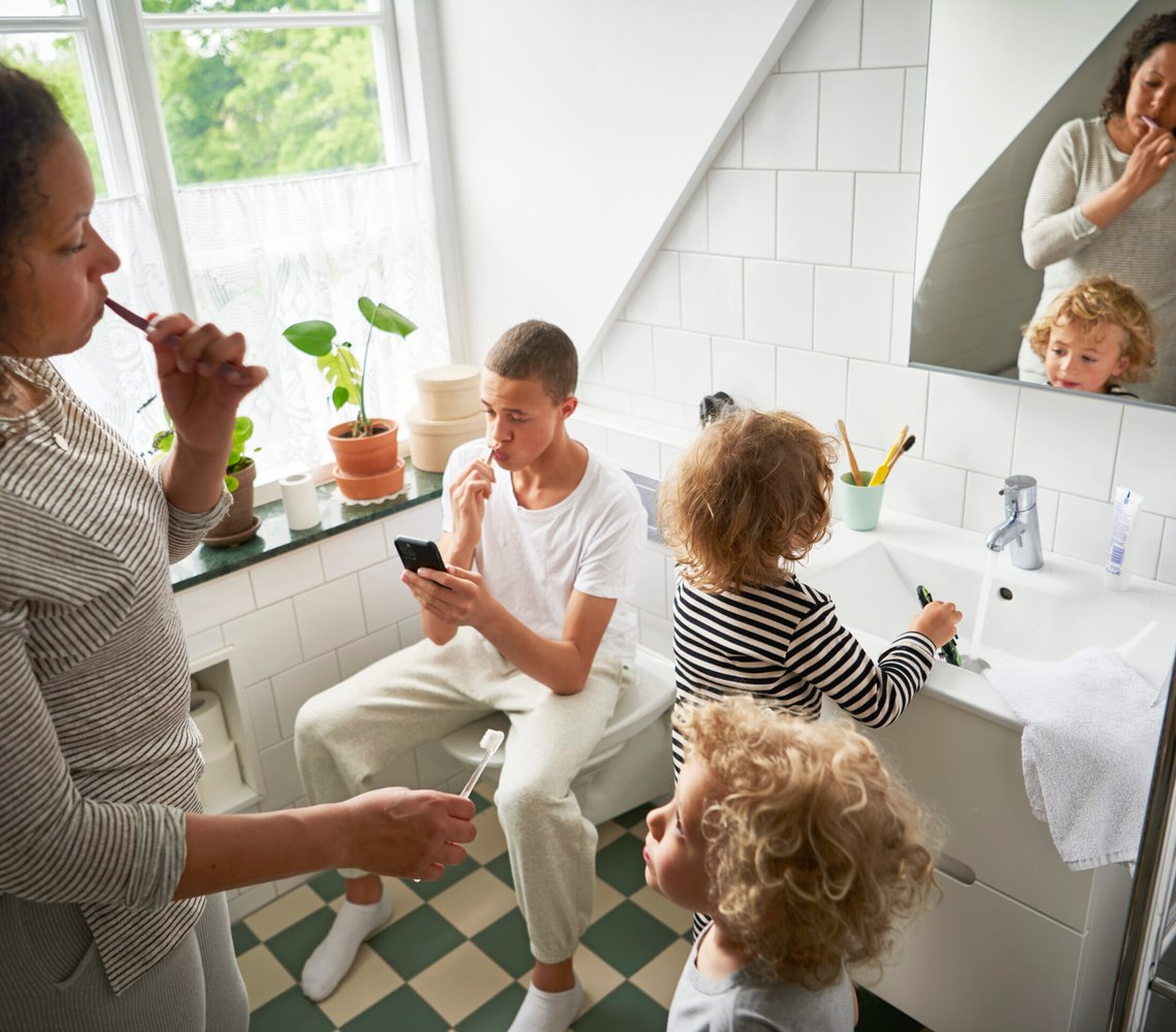 Mother and three children brush teeth in bathroom.