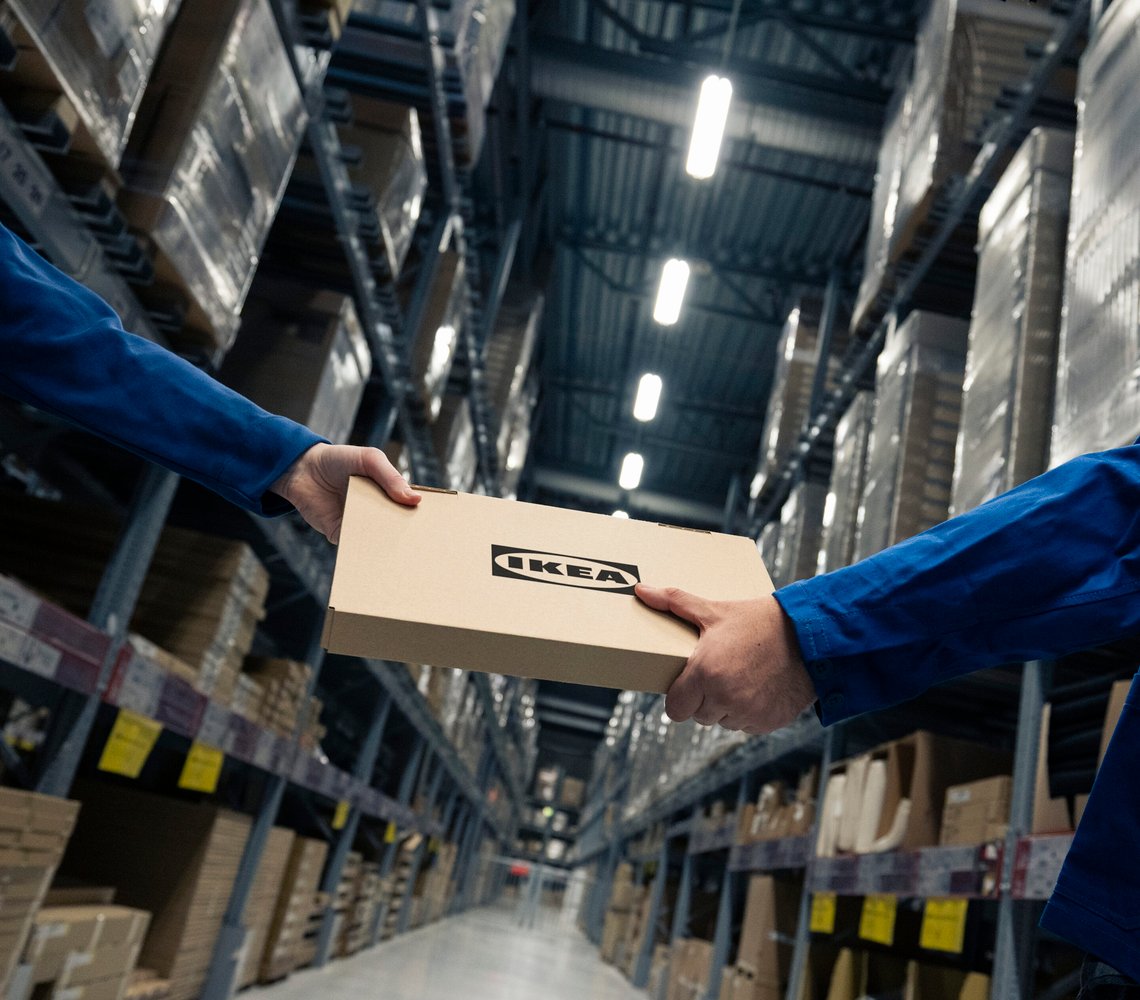 IKEA co-workers handling flat-pack box in warehouse.