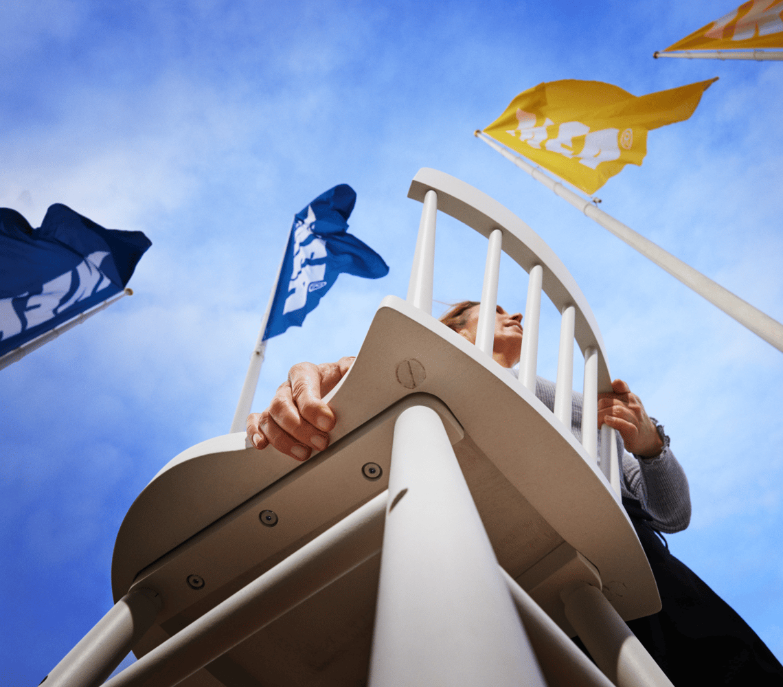 Woman carrying a chair with blue and yellow IKEA flags in the sky behind.