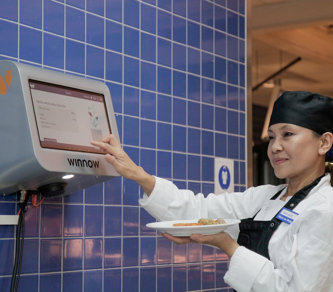 IKEA restaurant co-worker using Winnow digital food ordering system with blue tile wall.