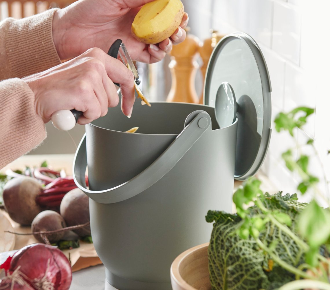 Person peeling potato over IKEA grey compost bin with lid in kitchen