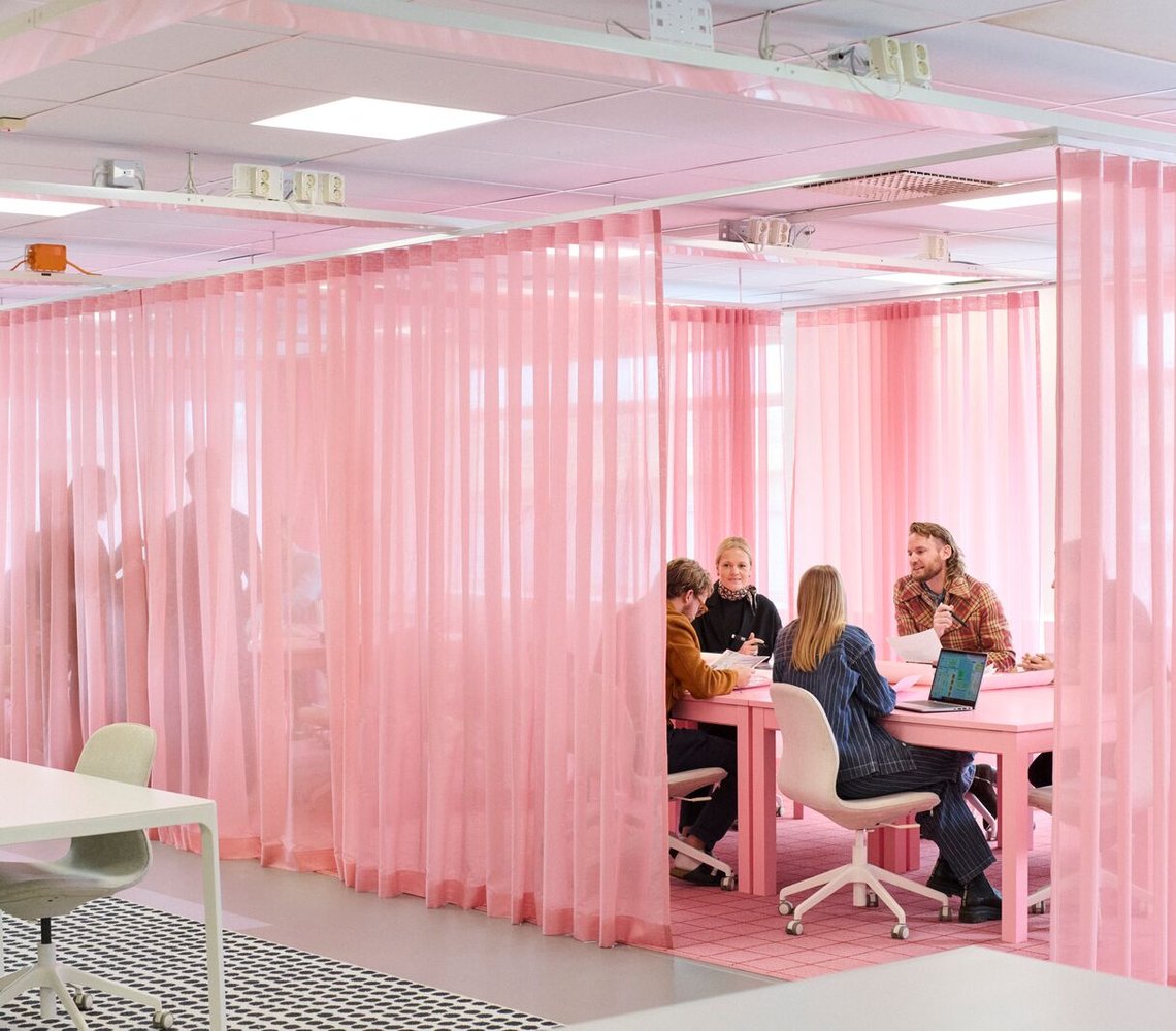 Co-workers in a meeting room with pink curtains.