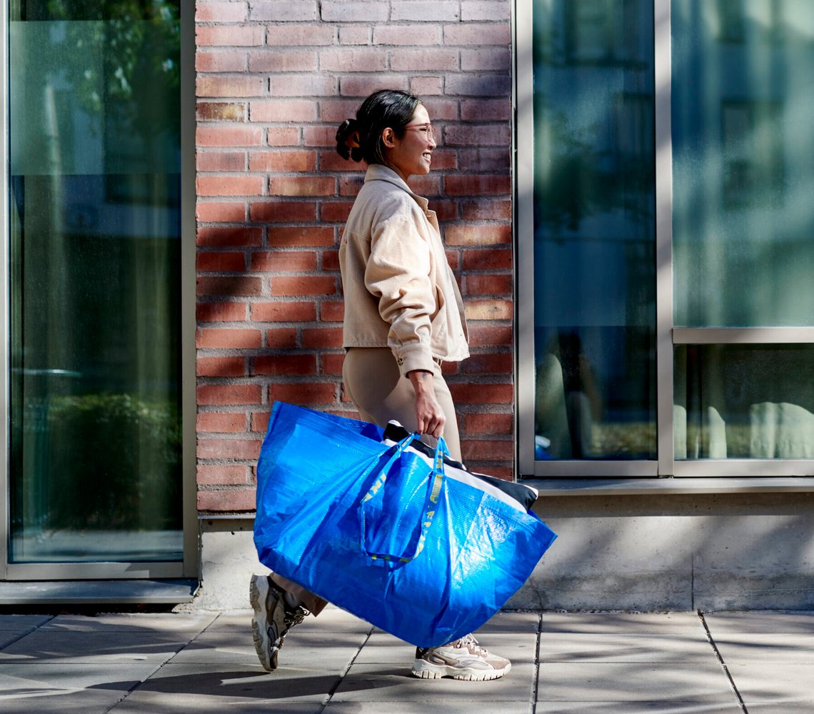 Woman leaving an IKEA Shop with her newly bought products in a FRAKTA bag.