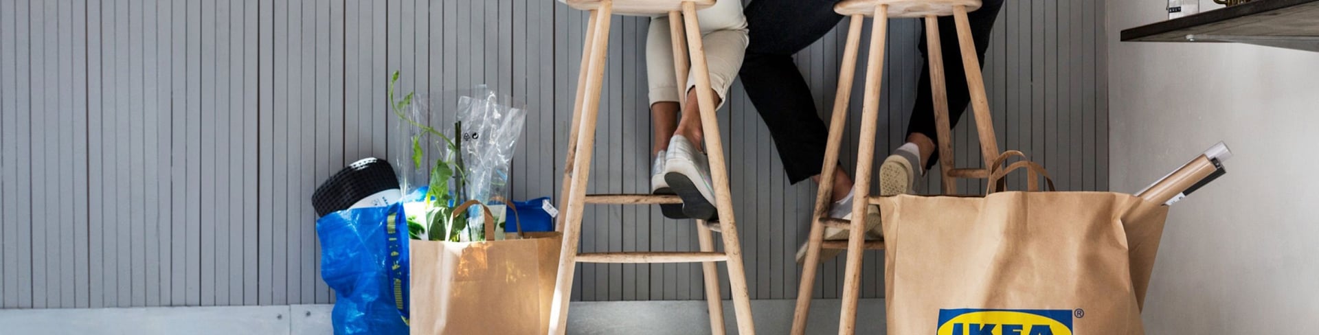 Two people sitting on stools with IKEA bags next to them
