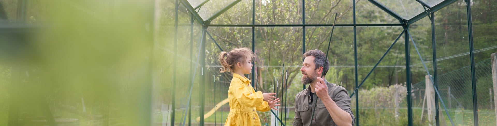 Father and daughter in a yellow dress and red rubber boots working together in a green house