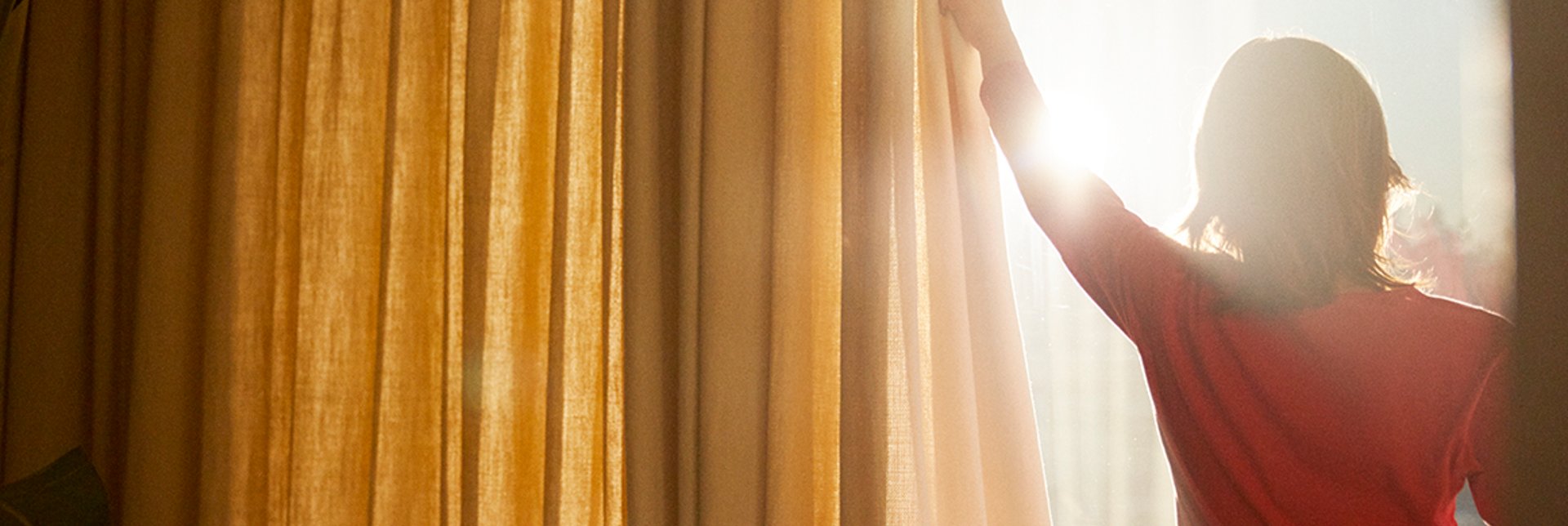 Person pulling curtains aside, allowing the sun to shine in through the windows.