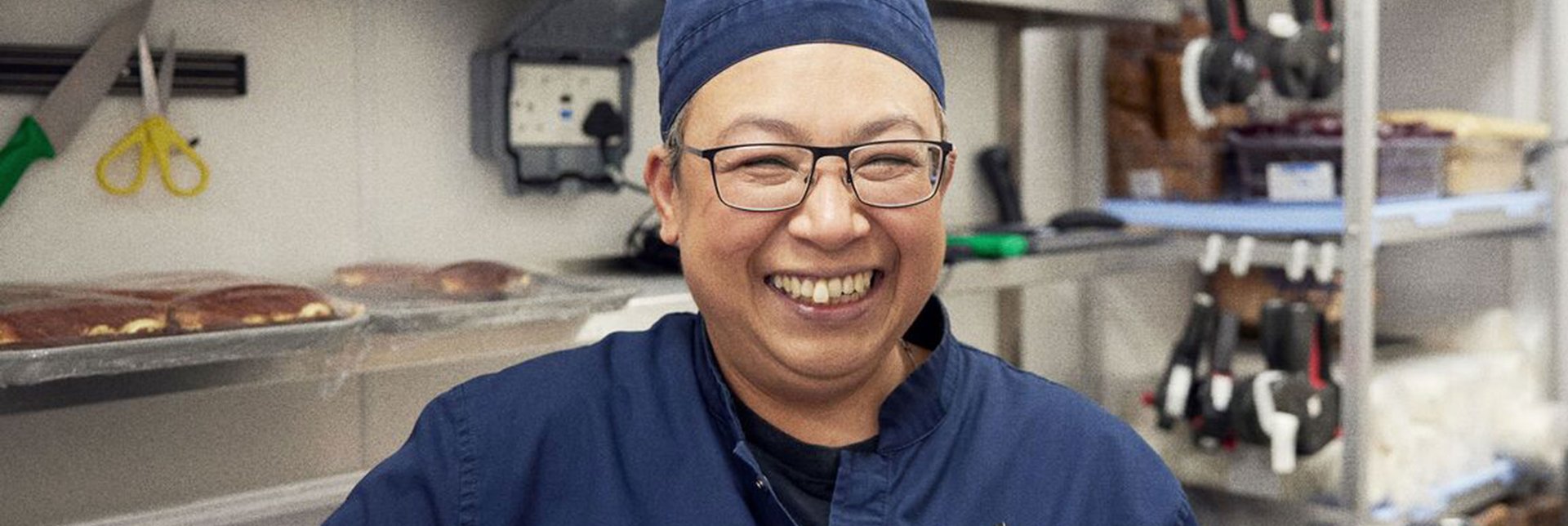 IKEA employee Nancy standing in the kitchen where she is the manager, wearing a blue work uniform smiling to the camera.