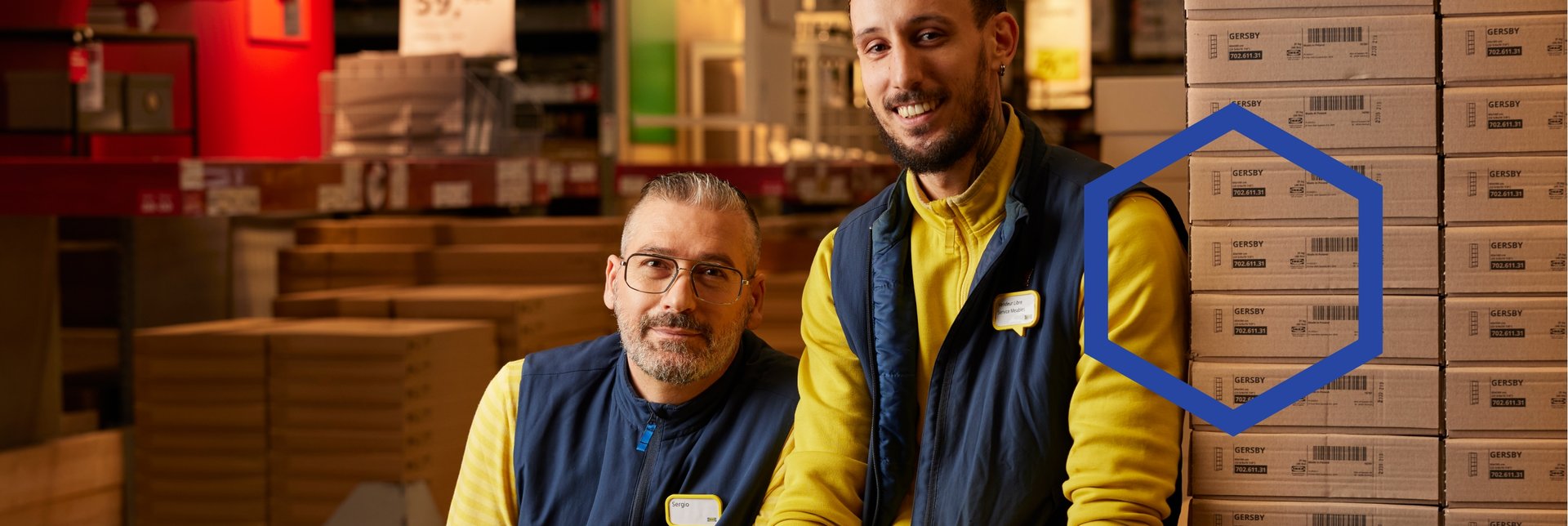 Two IKEA co-workers sitting on flat packs in a stores warehouse.
