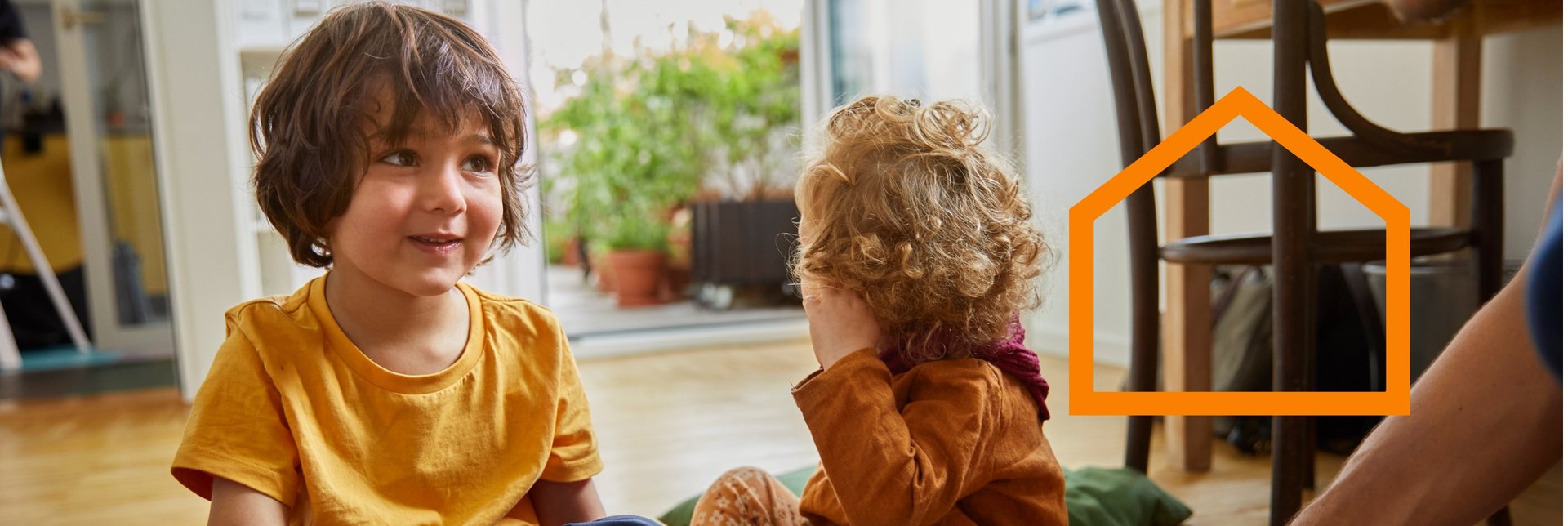 Two small children sits on the livingroom floor while their parent is assembling a piece of IKEA furniture.
