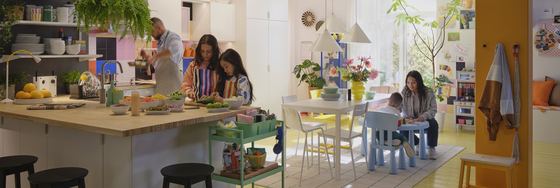 Family preparing food together in a colorful, modern IKEA kitchen and dining area, with open shelving, plants, and creative decor.