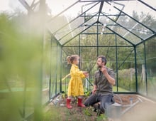 Father and daughter in a yellow dress and red rubber boots working together in a green house