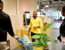 A smiling IKEA employee helping two customers in the self service check-out area.