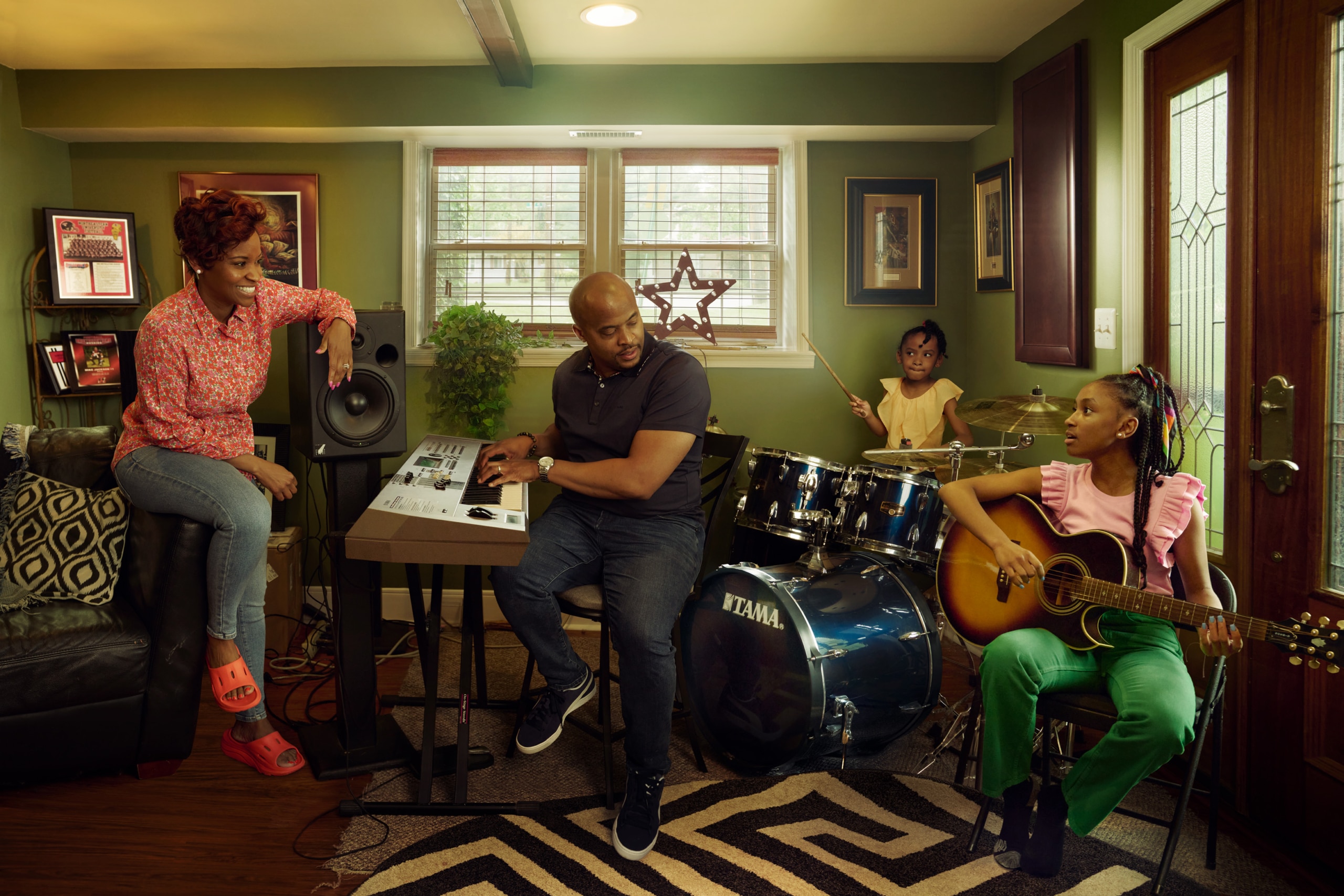 In the downstairs music room, Michael's playing a keyboard, his youngest daughter the drums, the oldest daughter an acustic guitar and his wife is sitting on an armchair listening.