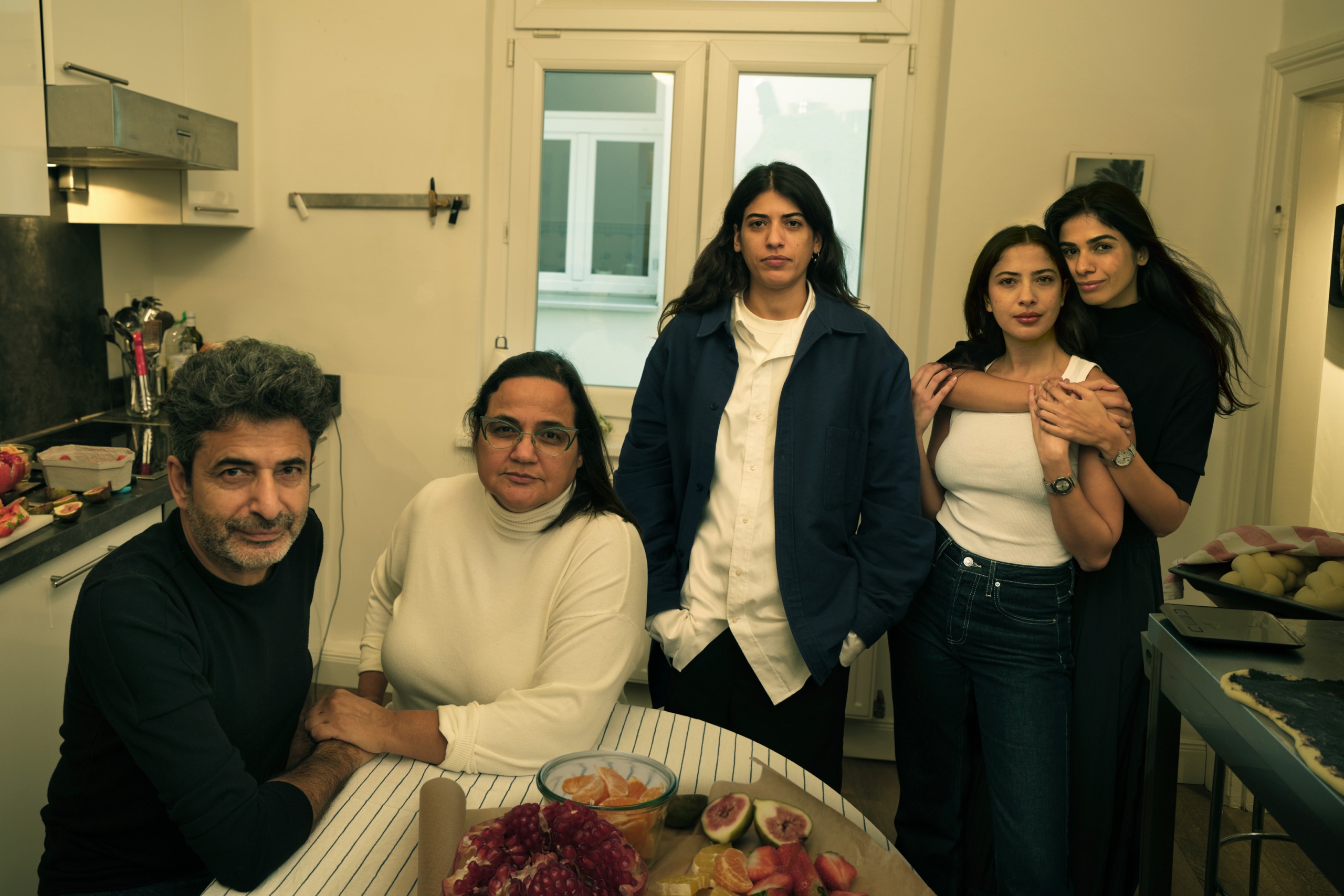 Toar in her kitchen, surrounded by friends, a plate of fruit is on the table.