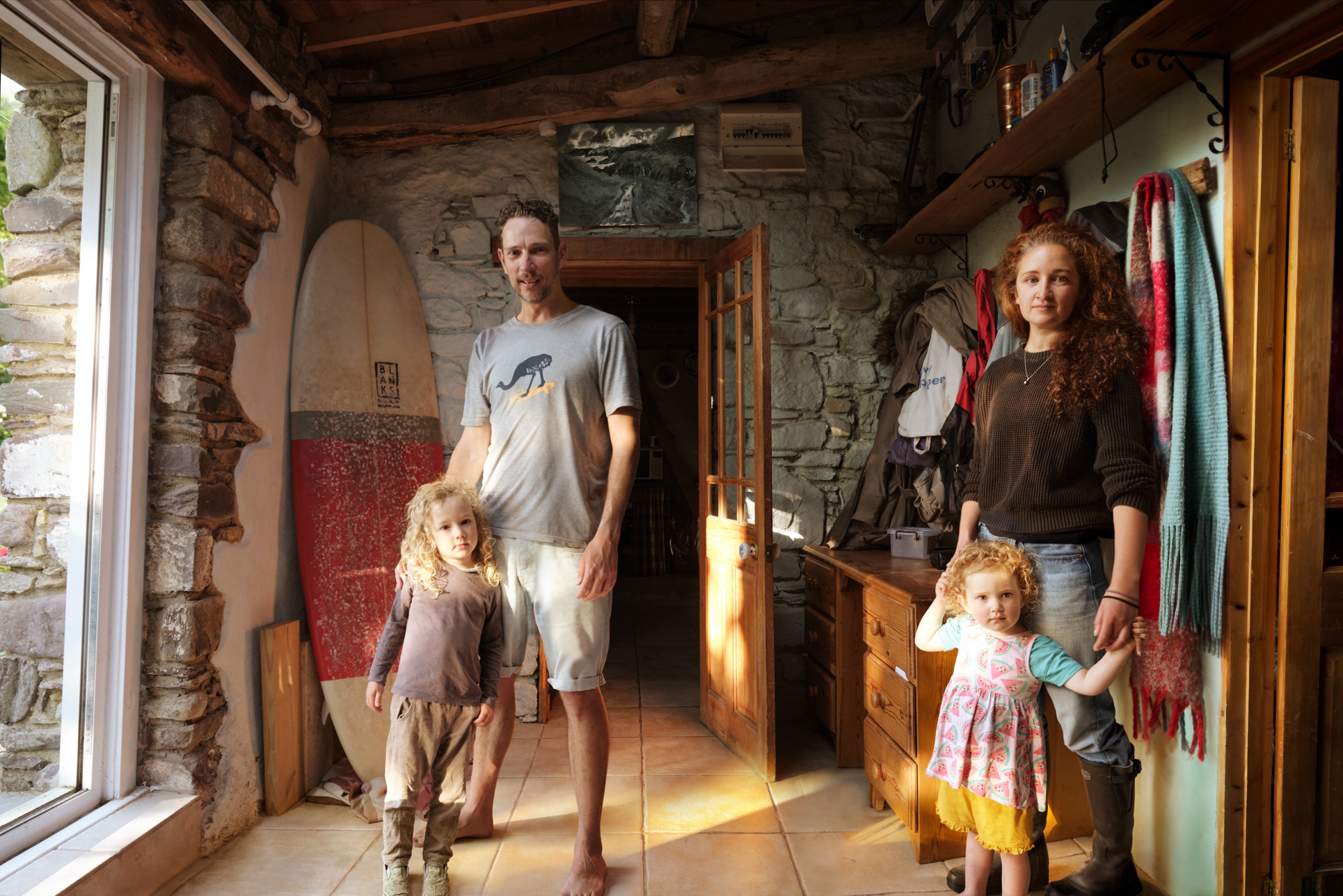 Francois, his wife and their daughers standing in the hallway, a surfboard is leaning on the wall behind him.