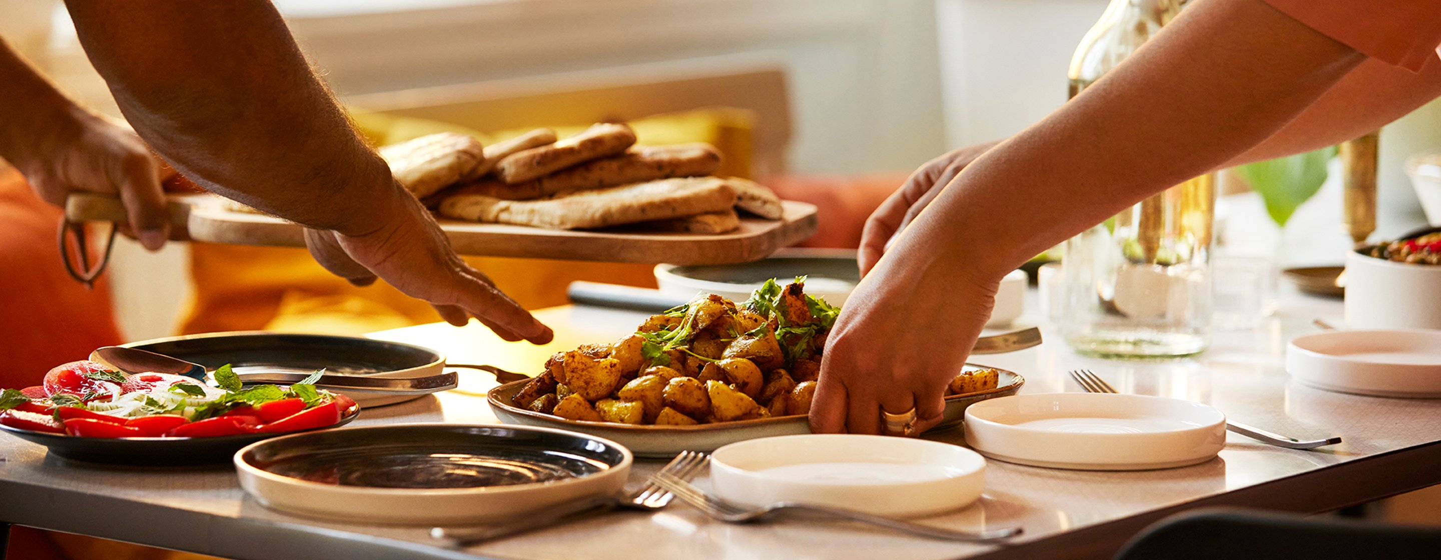 Focus on two peoples hands preparing plates of food on a kitchen table.