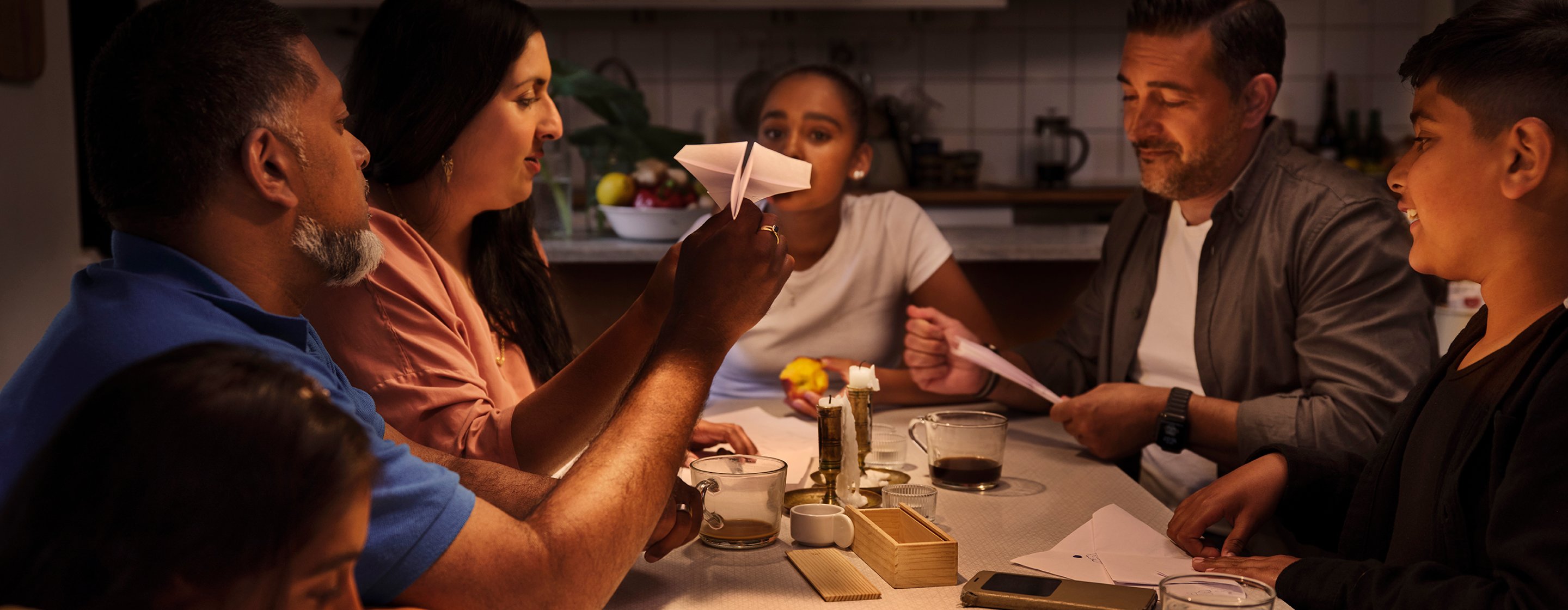 A family of six sitting by a kitchen table playing board games and chatting.