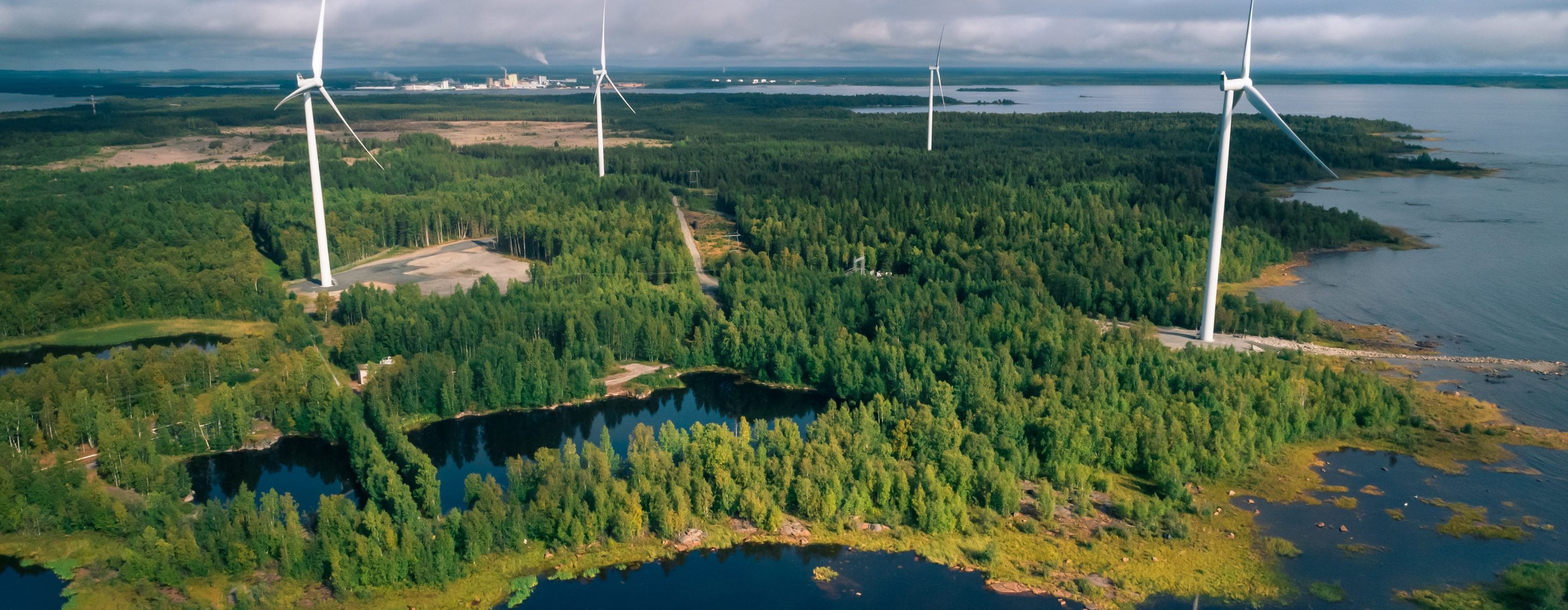 View over a windfarm in a forest by a shore in Finland.