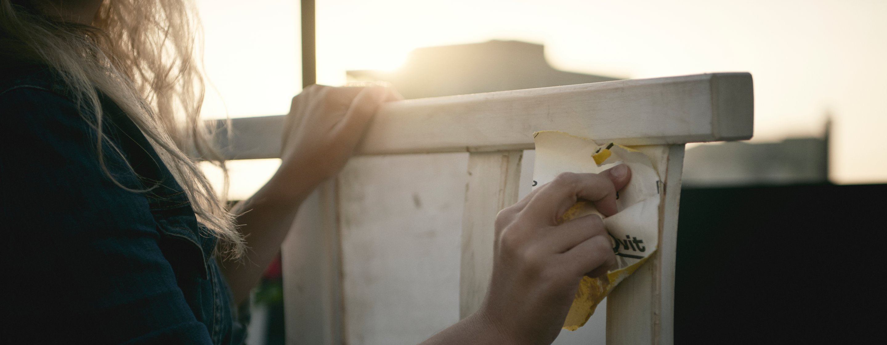 Woman sanding down a chair, giving it new life with a new coat of paint.