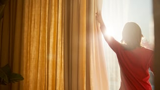 Person pulling curtains aside, allowing the sun to shine in through the windows.