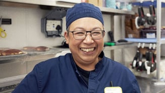 IKEA employee Nancy standing in the kitchen where she is the manager, wearing a blue work uniform smiling to the camera.