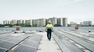 Man walking on a roof top with solar panels, high rise buildings in the background