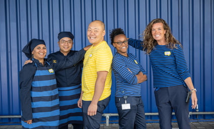 A group of IKEA co-workers smiling in front of a blue box store.