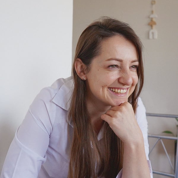 Nataliia wearing a white shirt sits in a bright room smiling.