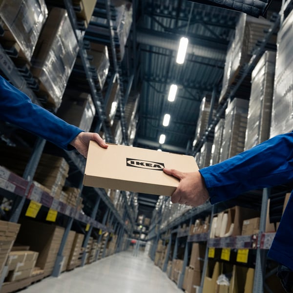 IKEA co-workers handling flat-pack box in warehouse.