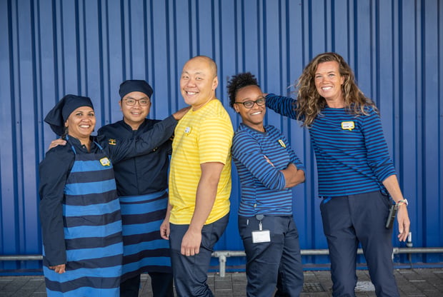 A group of IKEA co-workers smiling in front of a blue box store.