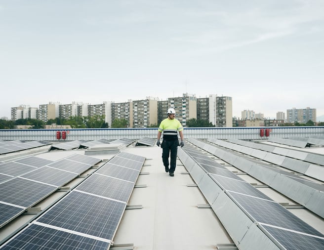 Man walking on a roof top with solar panels, high rise buildings in the background