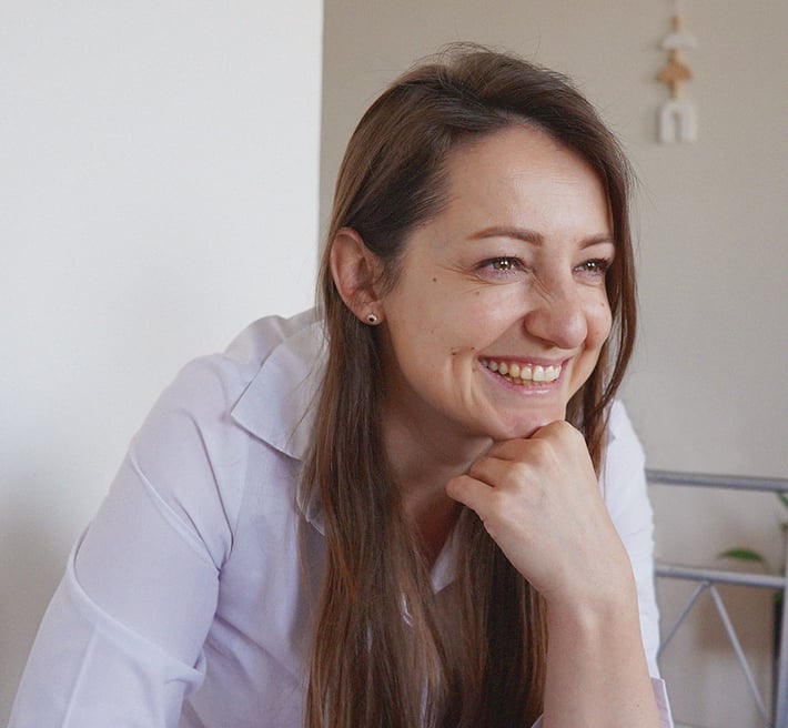 Nataliia wearing a white shirt sits in a bright room smiling.