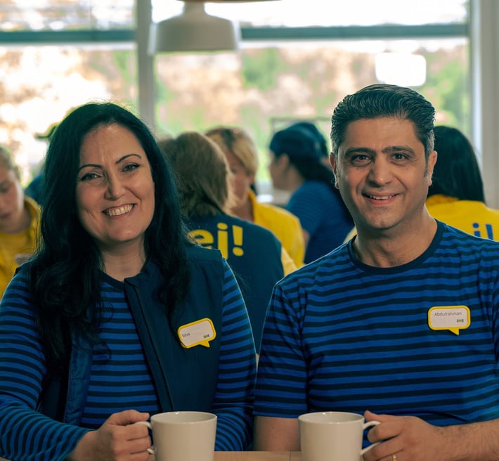 Silva and Abdul in their blue IKEA work wear sitting in the IKEA restaurant drinking coffee.
