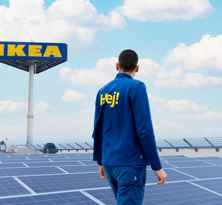 IKEA co-worker standing on rooftop solar panel installation with blue sky and IKEA sign.