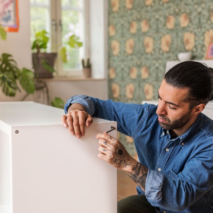 A man assembling a white KALLAX book shelf.