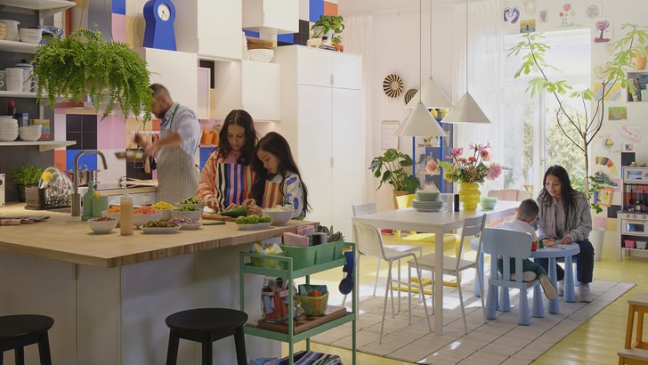 Family preparing food together in a colorful, modern IKEA kitchen and dining area, with open shelving, plants, and creative decor.
