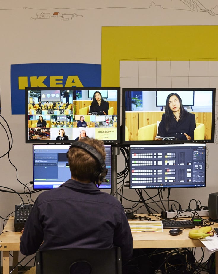 Over the shoulder image of person monitoring an ongoing panel discussion on several screens.