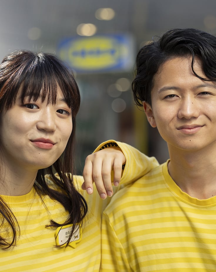 Two IKEA employees wearing yellow striped shirts and name tags, standing together outside an IKEA store.