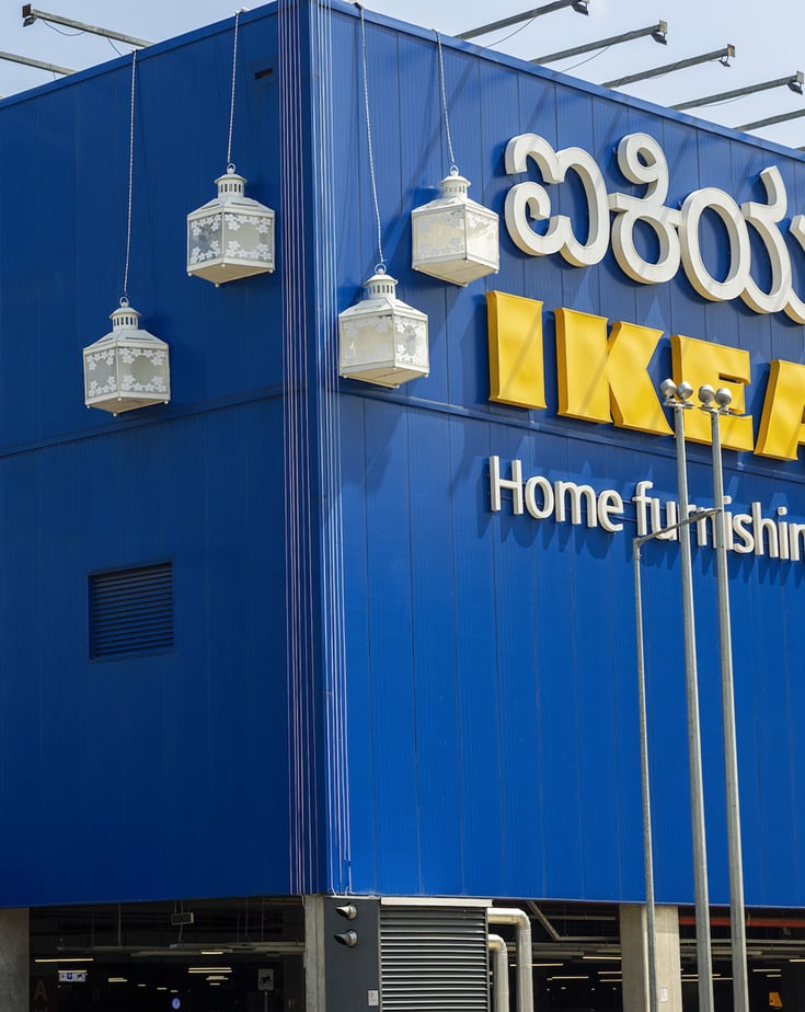 Exterior of an IKEA store with a blue facade, large yellow IKEA sign, and decorative white lanterns hanging on the building.