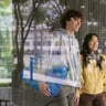 alttext Two people walking behind a window with a blue FRAKTA bag.