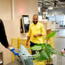alttext A smiling IKEA employee helping two customers in the self service check-out area.